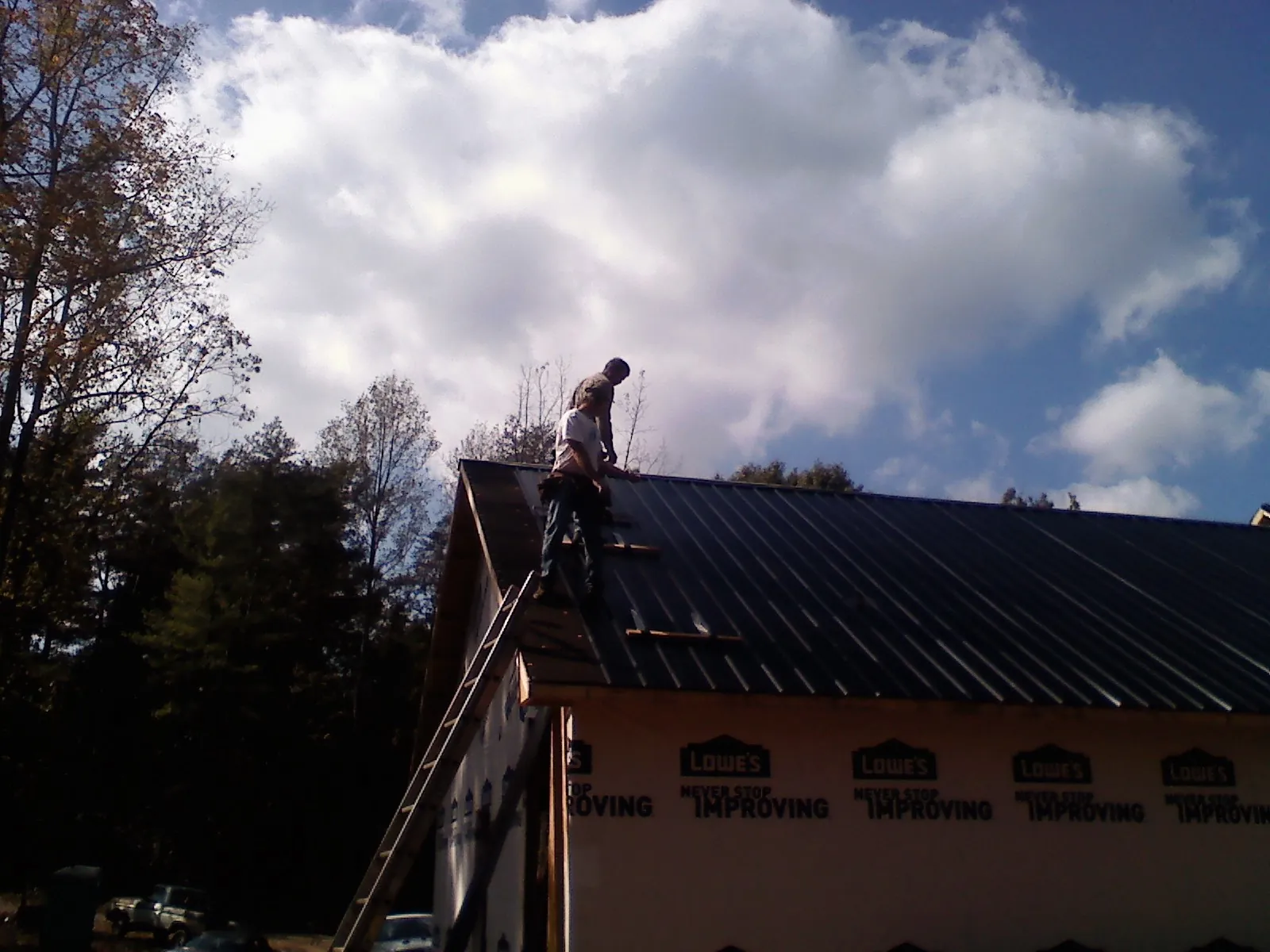 Roofer fastening dark metal panels high against a cloudy sky, from a Roof Inspection job in Malvern