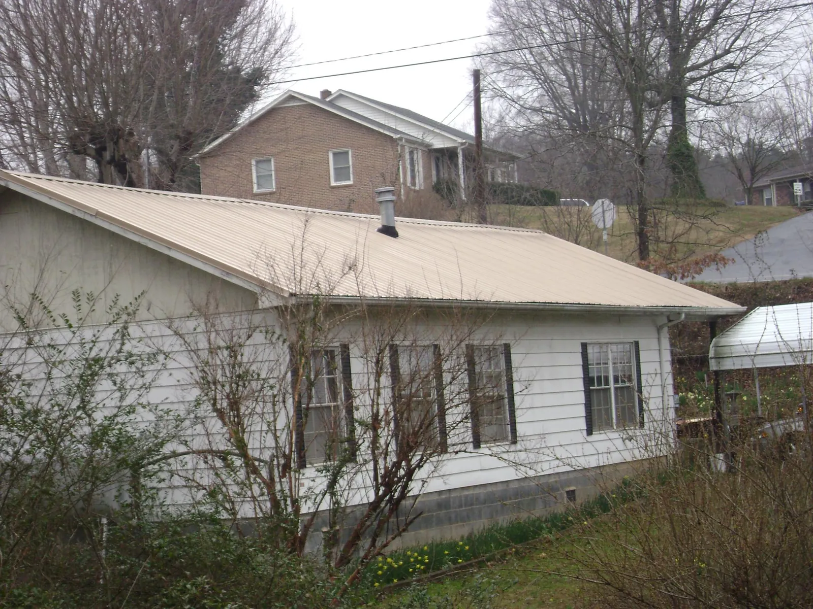 Tan metal roof on a white sided house set into a hillside — Commercial Roofing by Roofing Brothers in Malvern